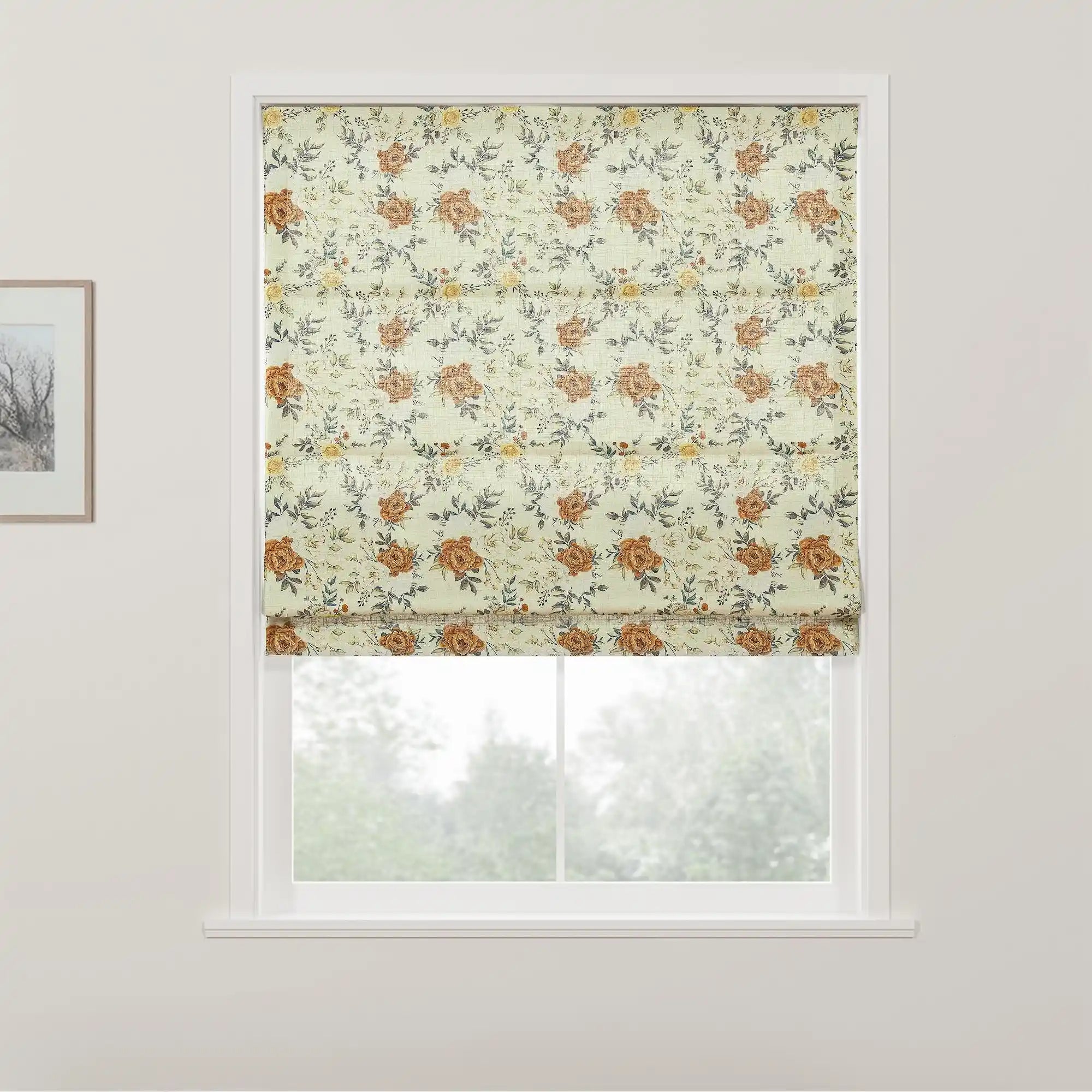 A Roman blind with a light cream background and an intricate floral pattern of rust orange roses yellow flowers and grey-green leaves hangs in a white-framed window overlooking blurred green foliage