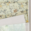 Textile fabric window blind with a vintage floral pattern featuring soft yellow roses muted blue-green leaves and rustic orange berries partially rolled up at an indoor window overlooking blurred green foliage