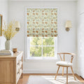 Photograph of an inviting room interior featuring a window with a floral roman shade in orange and yellow, a light wood dresser adorned with books and vibrant yellow blossoms, and a modern wishbone chair with a white cushion