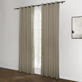 A pair of neutral beige grommet top blackout curtains hang on a black rod in a modern room with a white wall, dark wood floor, and an abstract black and white painting visible