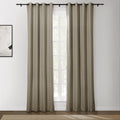 A pair of long greige grommet blackout curtains on a black rod in a modern room with a bright window, an abstract white art print, and a woven beige rug on a dark wood floor
