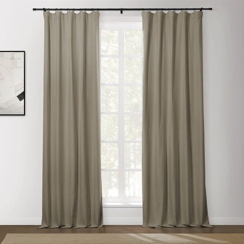 A pair of taupe grommet curtains on a black rod flanking a bright multi-paned window in a modern room with abstract wall art and a beige textured rug