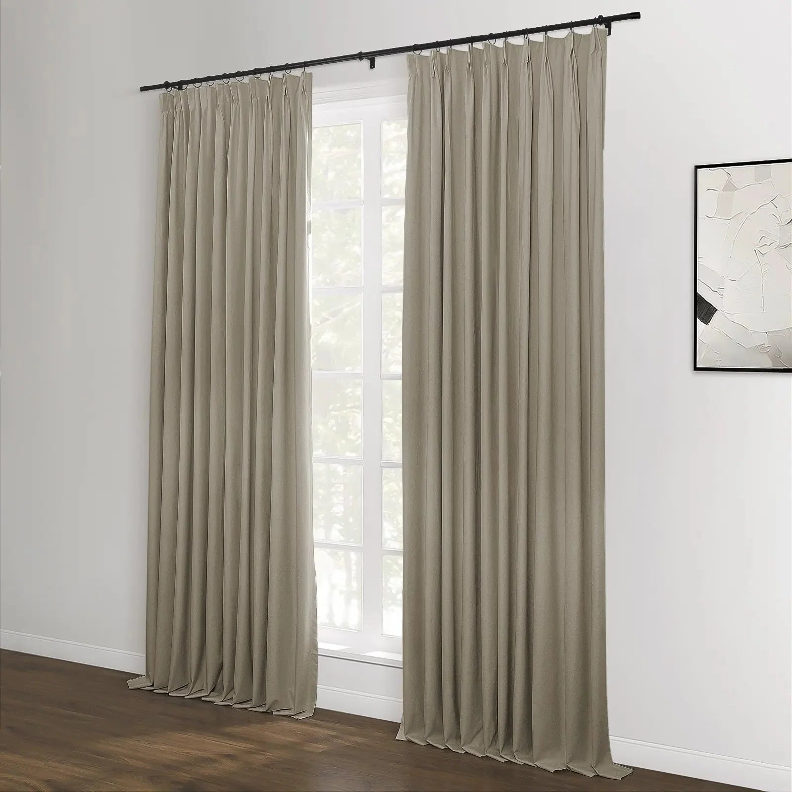 Pair of beige floor-length curtains suspended from a black rod with rings in a contemporary room, framing a white-paned window, complemented by dark hardwood floors and an abstract black and white artwork on the adjacent wall