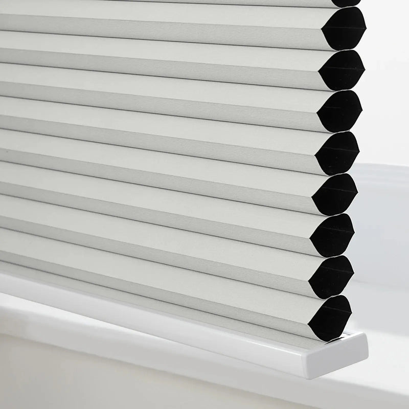 Photograph of a light grey cellular window Blind with visible black interior cells resting on a white windowsill