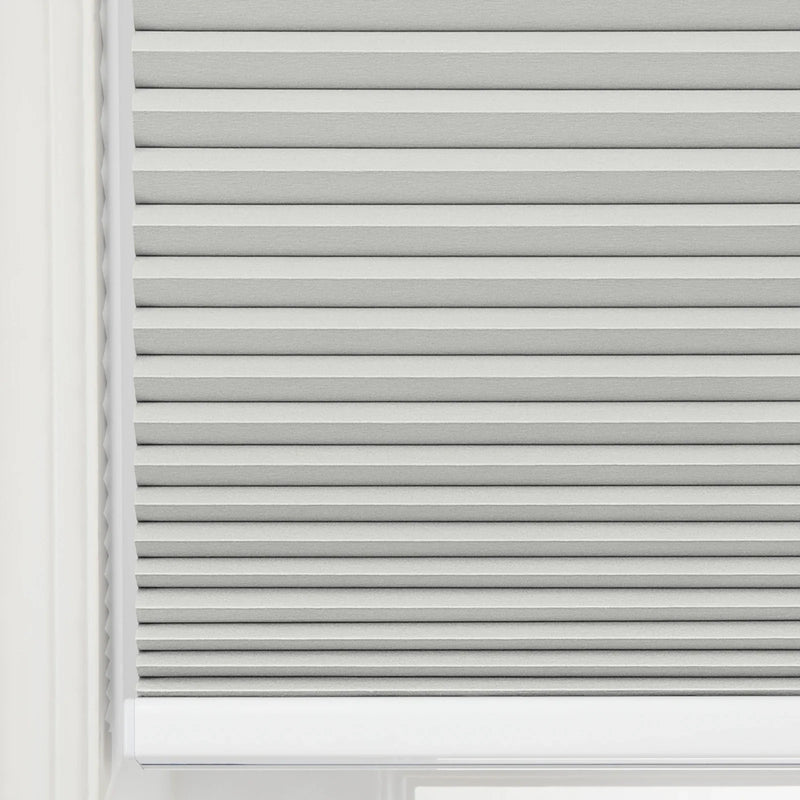 Close-up of a light grey pleated Blind featuring distinct horizontal folds and a subtle textured fabric set within a bright white window frame