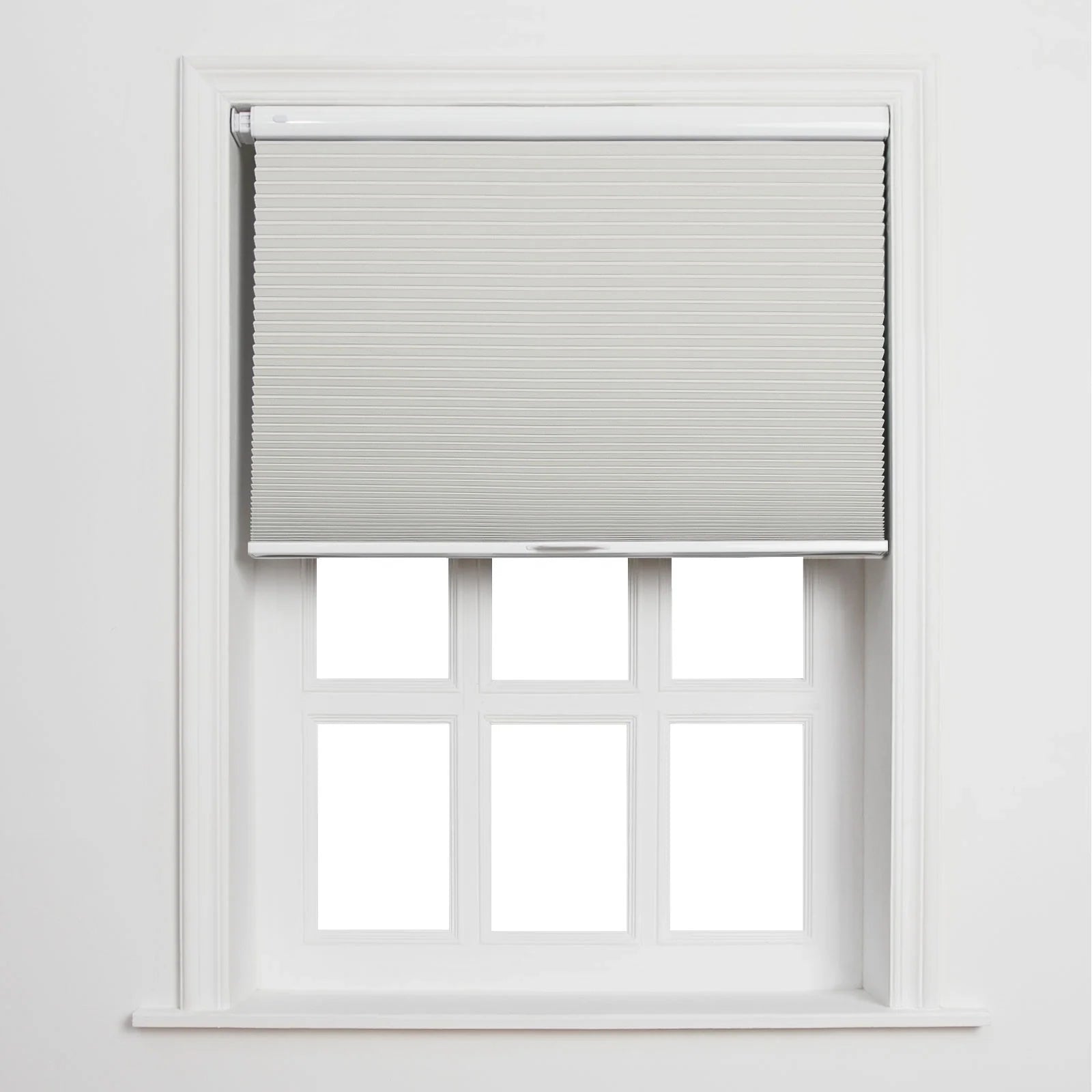 A clean interior image of a white window featuring a light gray pleated cellular Blind partially raised above six bright white panes, set against a minimalist white wall