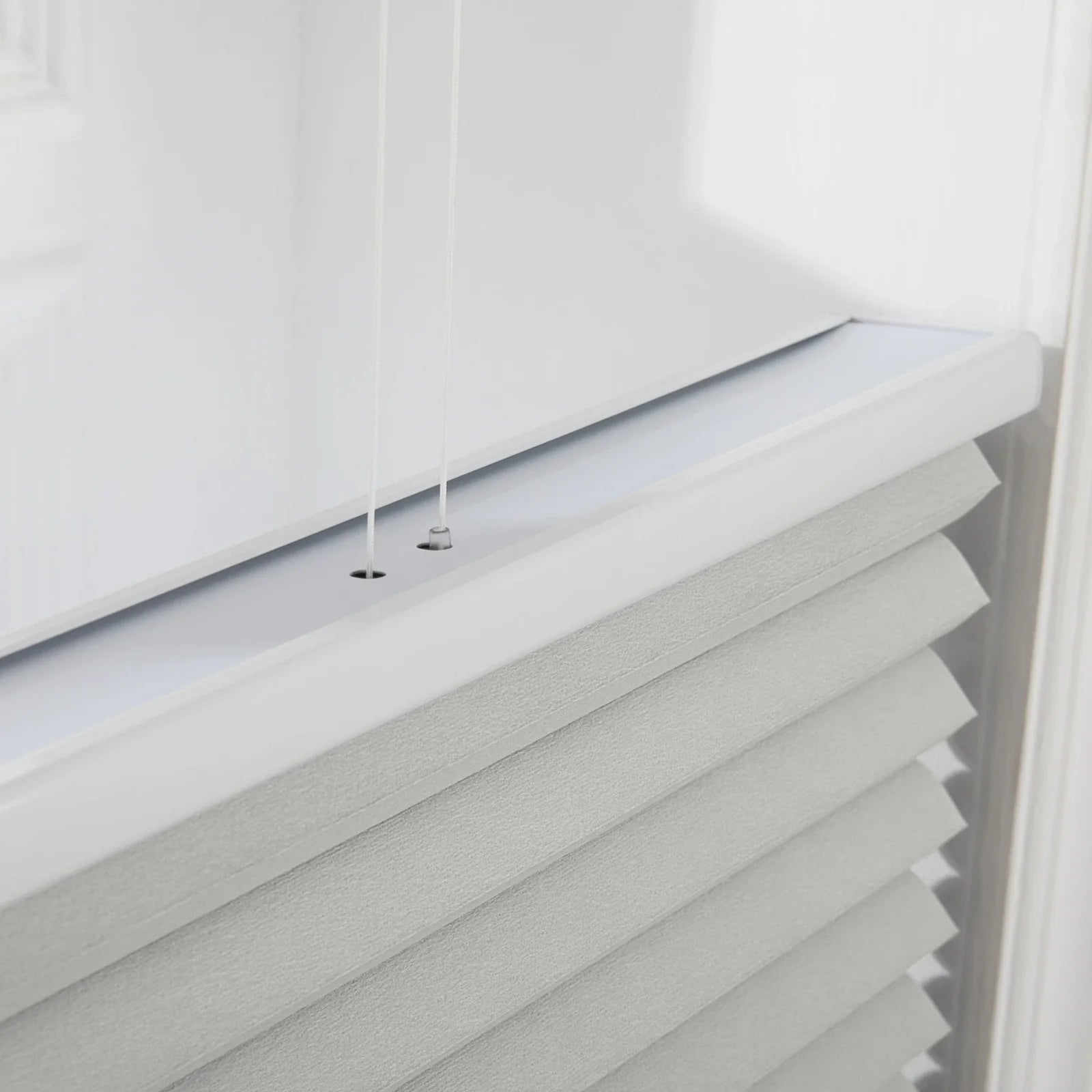 Photography of modern white pleated cellular Blinds on an interior window, featuring a crisp white top rail, two thin control cords, and textured gray-white fabric