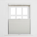 Photography of a clean white multi-pane window with a light grey cellular honeycomb Blind pulled halfway down and visible control cords against a simple white wall