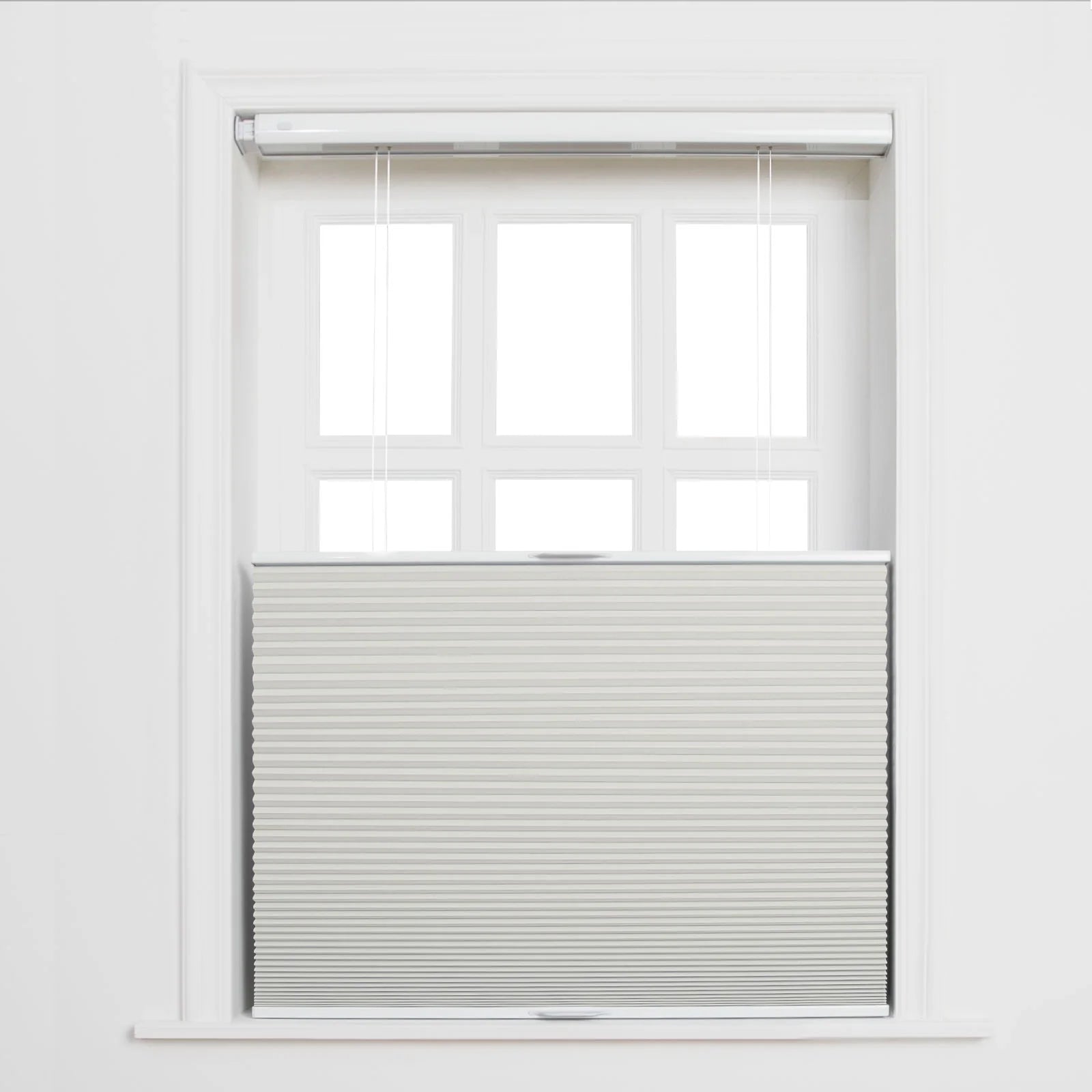 Photography of a clean white multi-pane window with a light grey cellular honeycomb Blind pulled halfway down and visible control cords against a simple white wall