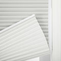 A close-up of a partially rolled light grey cellular pleated window Blind revealing its accordion-like structure, next to a soft white sheer curtain
