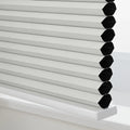 Close-up of light grey textured cellular Blinds on a white windowsill revealing the insulating honeycomb structure with black interiors for room darkening