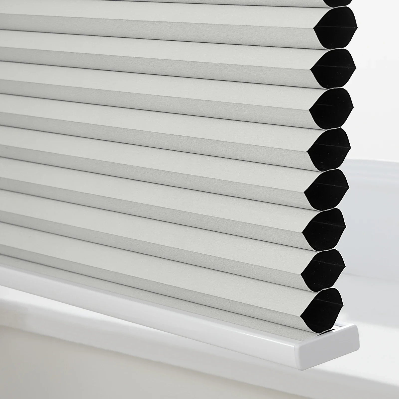 Close-up of light grey textured cellular Blinds on a white windowsill revealing the insulating honeycomb structure with black interiors for room darkening