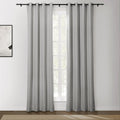 Photograph of light gray grommet top curtains on a black rod framing a window in a bright room, with an abstract white and black artwork on the wall and a brown textured rug on the wooden floor