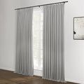 Photograph of light gray pleated curtains on a black rod over a large window showing green trees, with a textured white abstract artwork on the adjacent white wall