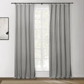 Light grey panel curtains hang from a black rod with rings covering a white-framed window in a room with an abstract white and black artwork and a textured brown rug