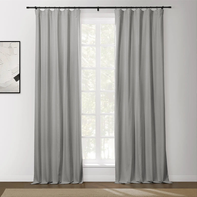 Light grey panel curtains hang from a black rod with rings covering a white-framed window in a room with an abstract white and black artwork and a textured brown rug