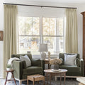 Light Khaki Liz Linen Pleated Curtains framing a green sofa beneath a wide sunlit window