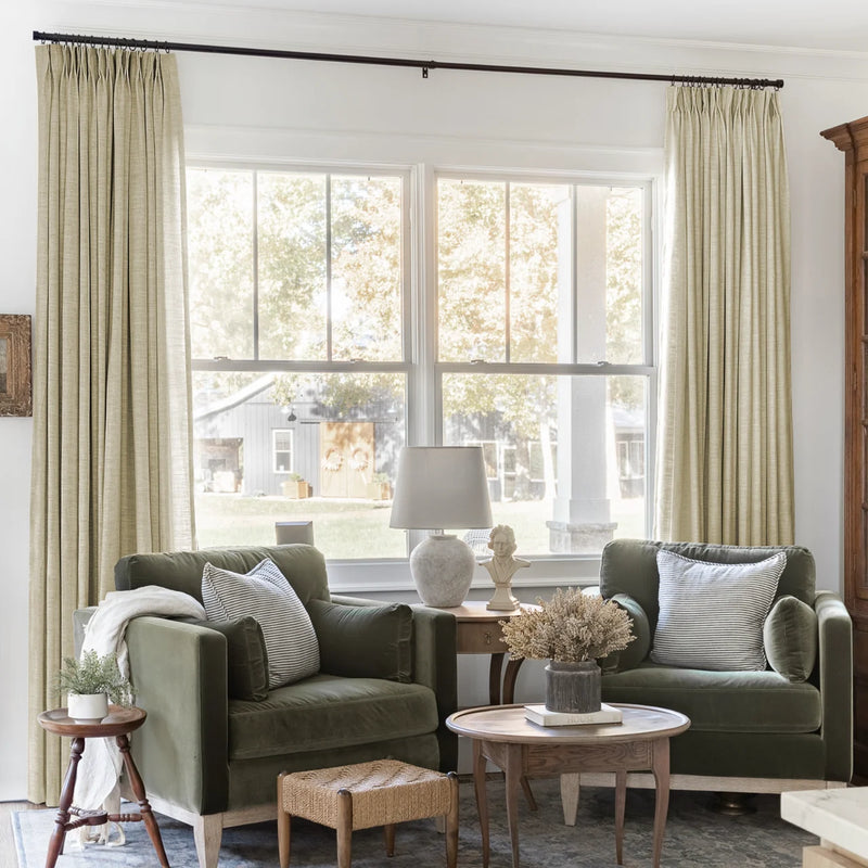 Light Khaki Liz Linen Pleated Curtains framing a green sofa beneath a wide sunlit window