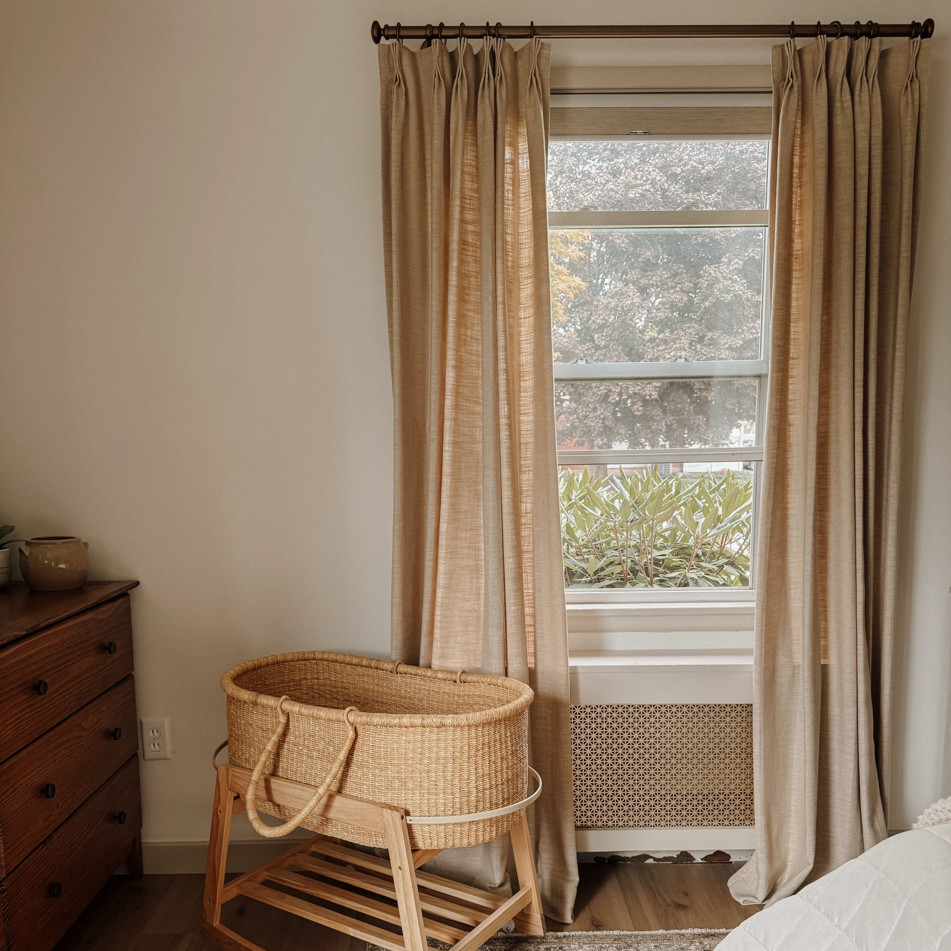 Light Khaki Liz Linen Pleated Curtains in a bedroom beside a rattan bassinet and wooden chest