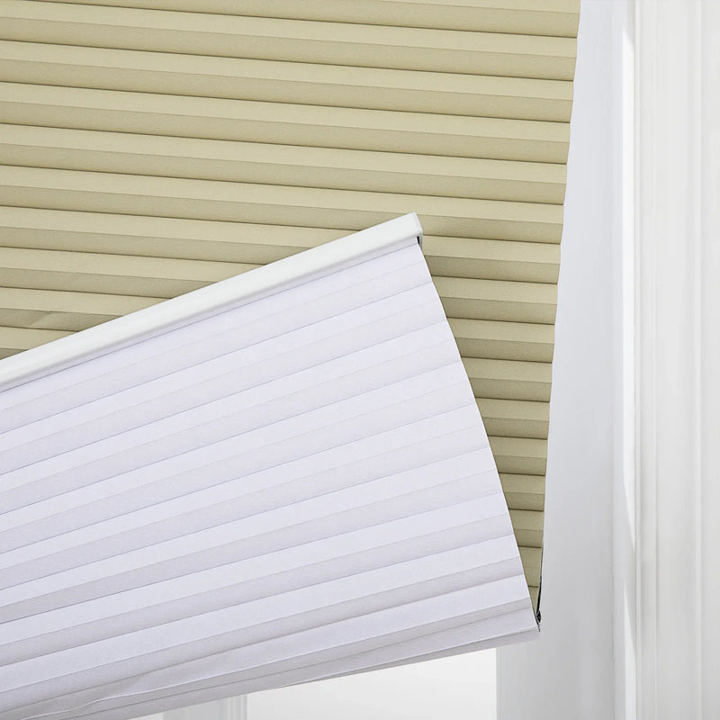 A white cellular Blind angled downward in front of a beige pleated Blind with a white window frame visible on the right