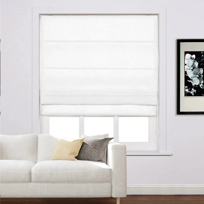 A white Roman blind covering a window in a bright living room, featuring a white sofa with a yellow cushion and a grey patterned cushion, alongside a framed black and white floral art print