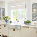 A bright white kitchen interior featuring a farmhouse sink with a brass faucet, white subway tile backsplash, white shaker cabinets with brass hardware, and blue and white chinoiserie decor including a vase of white hydrangeas