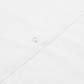 Photograph of a close-up white linen fabric detail featuring a single light-colored pearl button on a diagonal seam