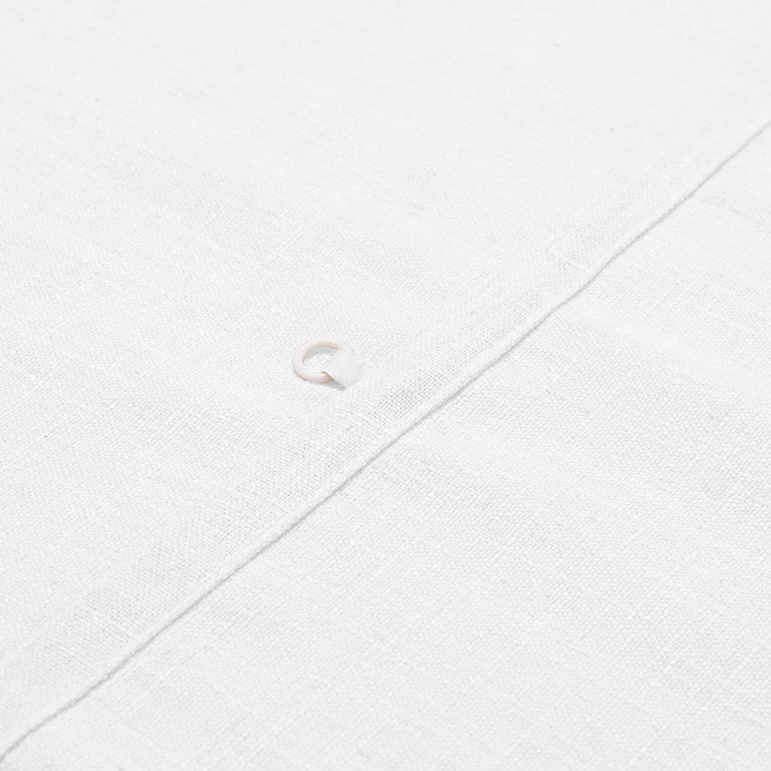 Photograph of a close-up white linen fabric detail featuring a single light-colored pearl button on a diagonal seam