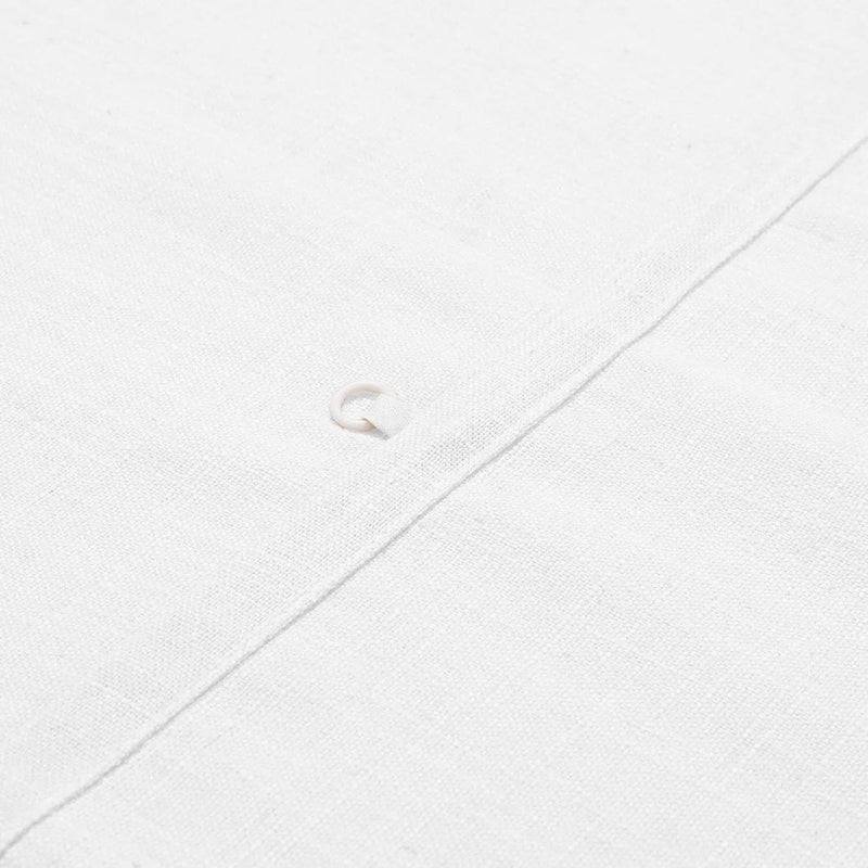 Photograph of a close-up white linen fabric detail featuring a single light-colored pearl button on a diagonal seam