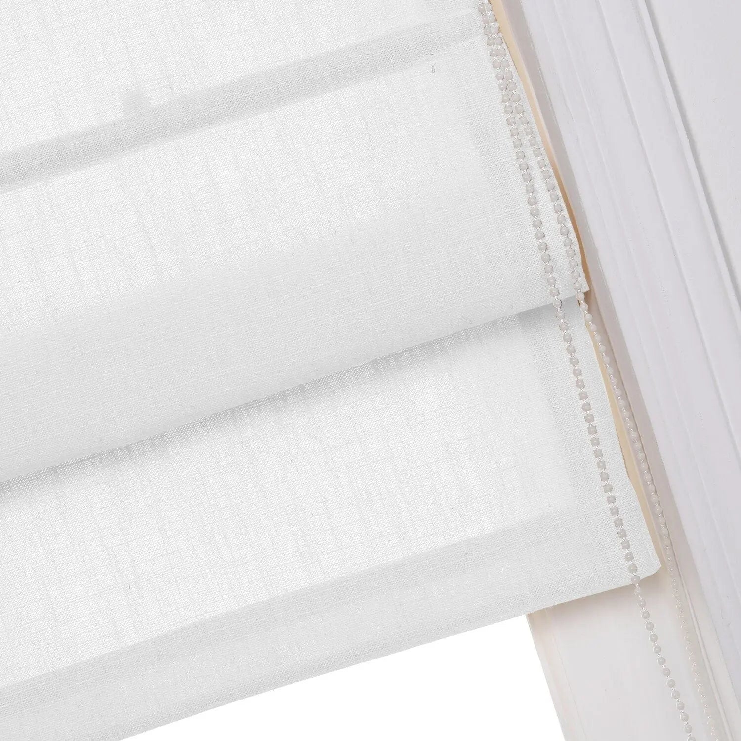 Close-up view of a white linen-textured Roman blind showing soft horizontal folds and a pearl-like beaded chain mechanism for adjustment