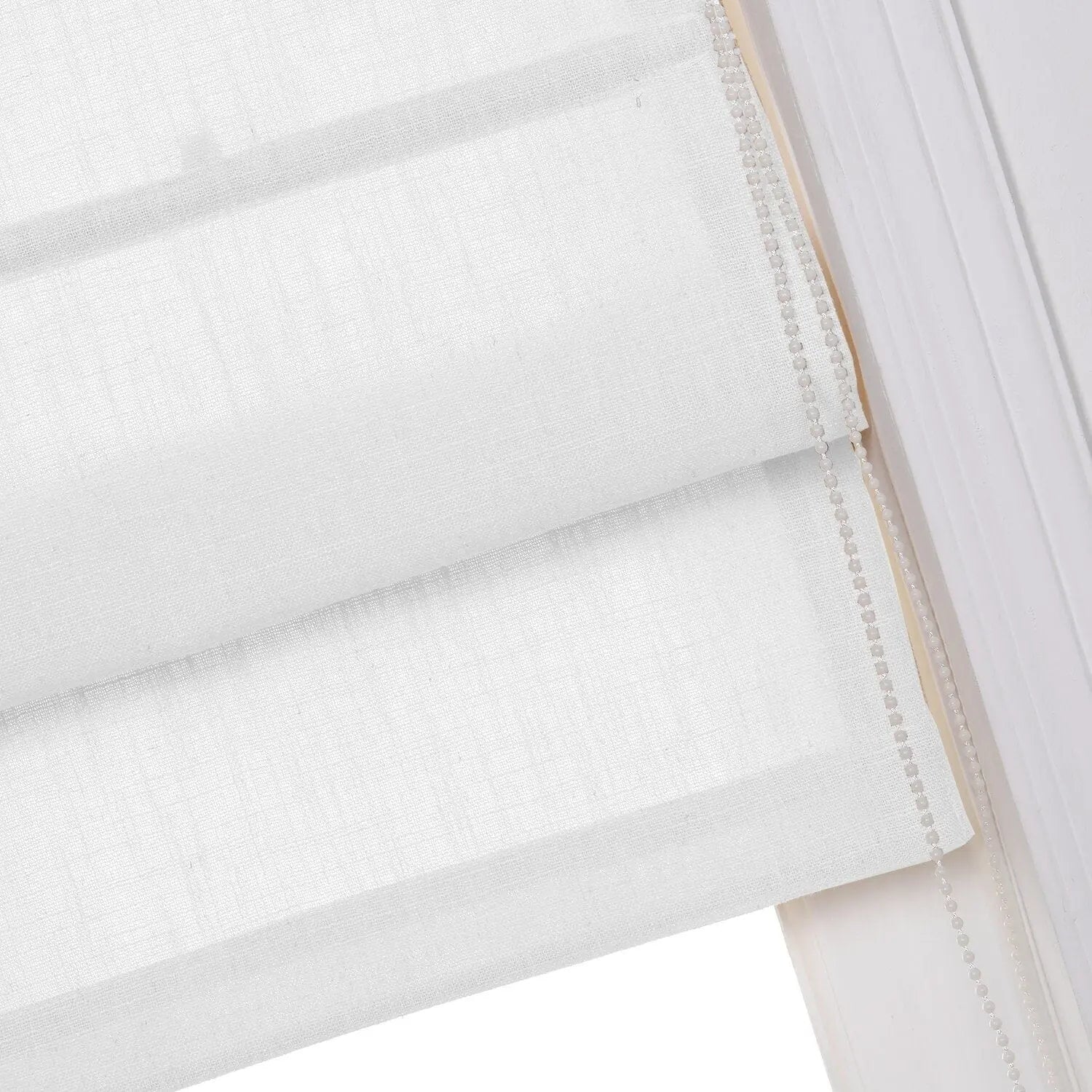 Close-up of white textured linen Roman window blinds showing soft horizontal folds and a translucent beaded pull chain