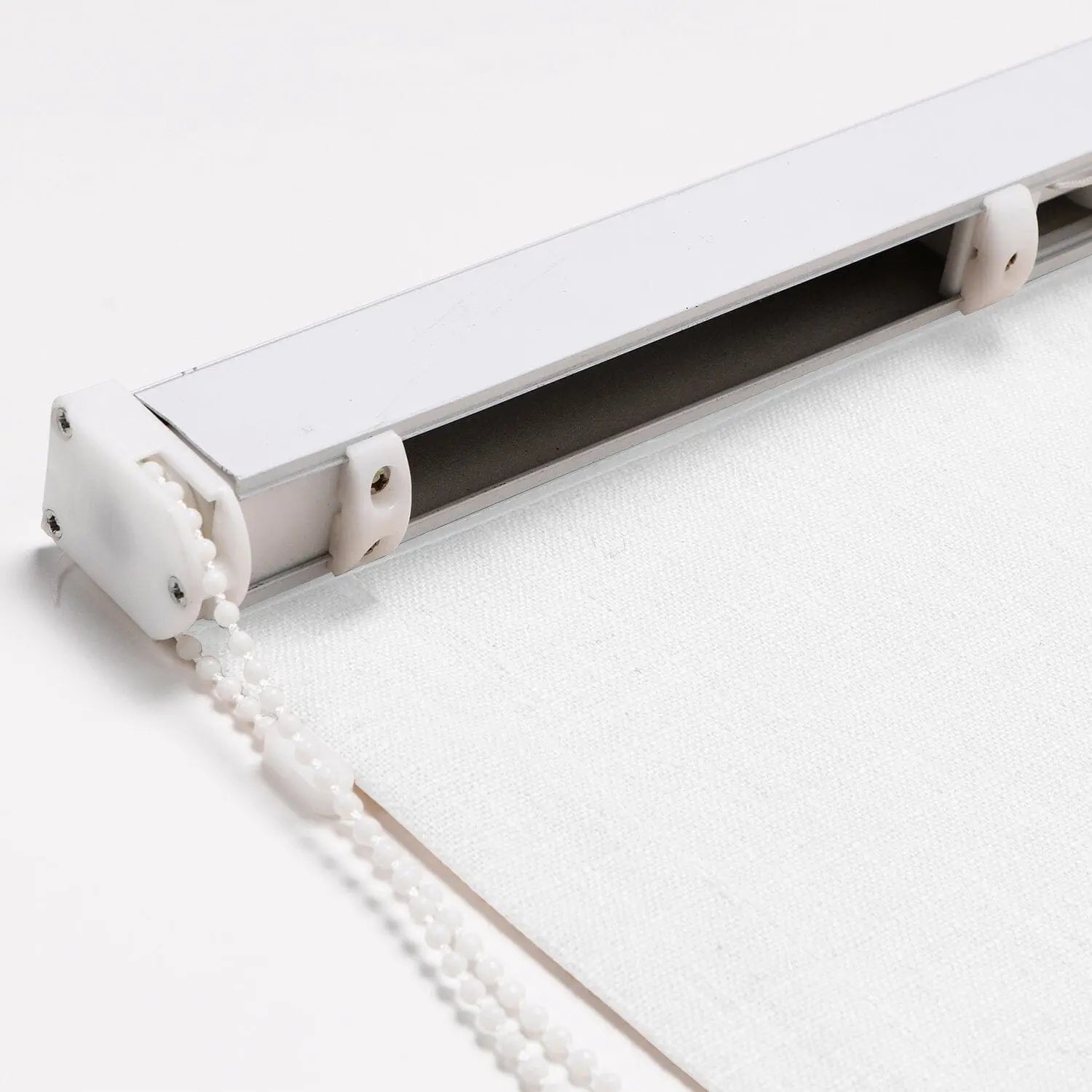 Photograph of a white roller blind mechanism showing a white aluminum rail a plastic beaded chain and textured white fabric