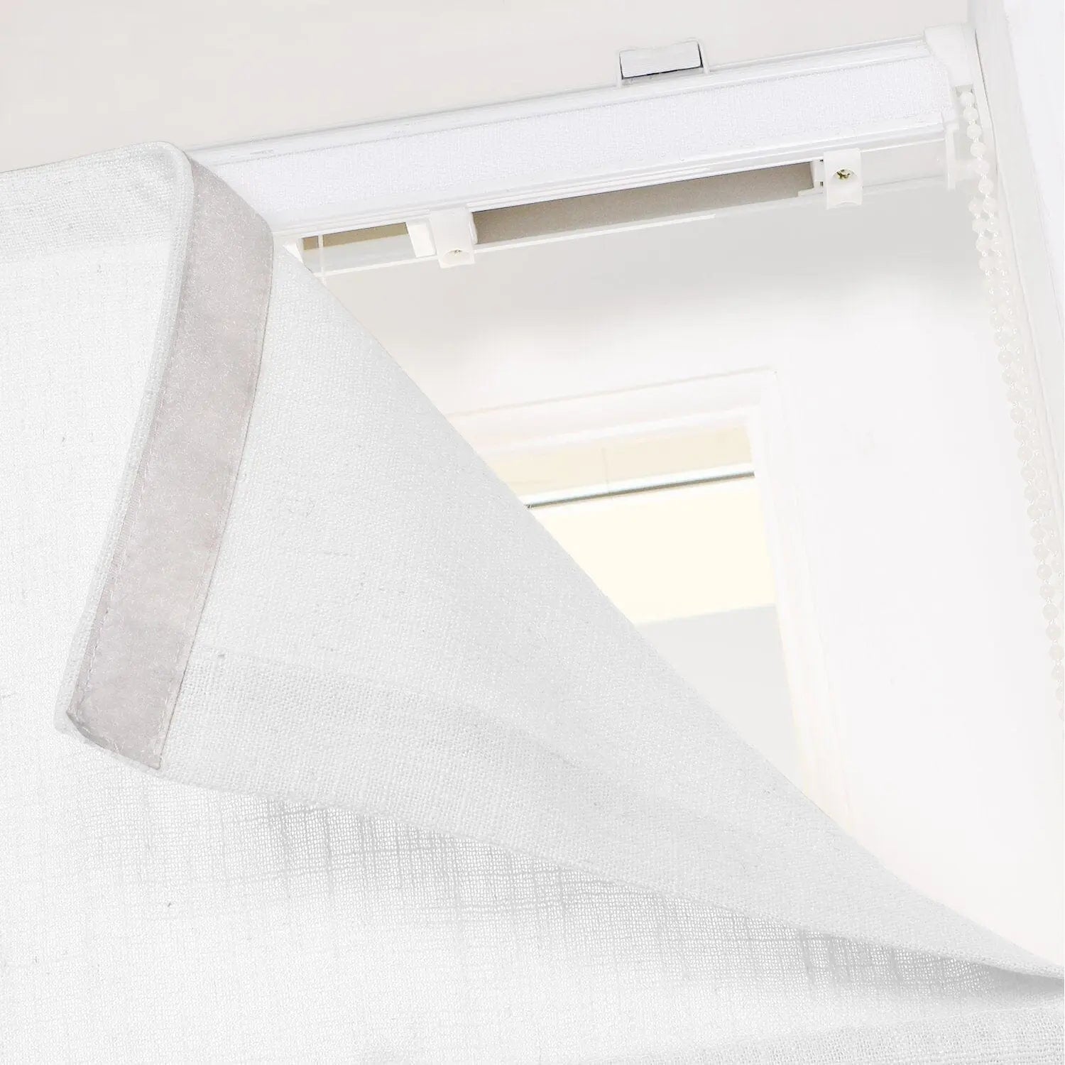 White textured fabric window blind being adjusted, revealing its top rail system with white plastic mounting clips and a beaded control chain on the right