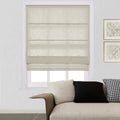 A modern living room interior features a window with light beige textured Roman blinds, a cream textured sofa with a black and a houndstooth cushion, and two framed abstract artworks on the white wall