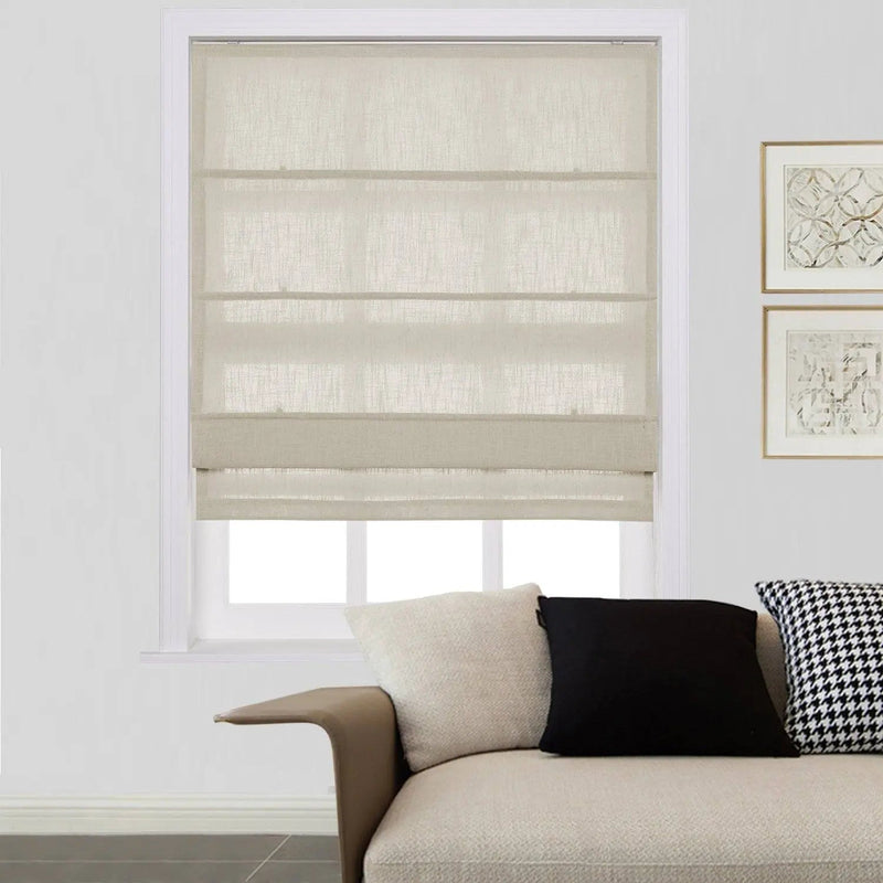 A modern living room interior features a window with light beige textured Roman blinds, a cream textured sofa with a black and a houndstooth cushion, and two framed abstract artworks on the white wall