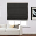 Black fabric roman shade covering a window in a modern living room featuring a white sofa with light yellow and charcoal grey throw pillows and a black framed floral art piece
