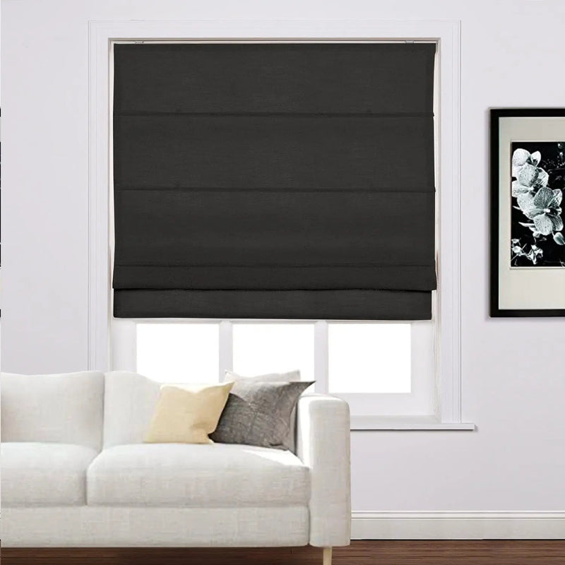 Black fabric roman shade covering a window in a modern living room featuring a white sofa with light yellow and charcoal grey throw pillows and a black framed floral art piece