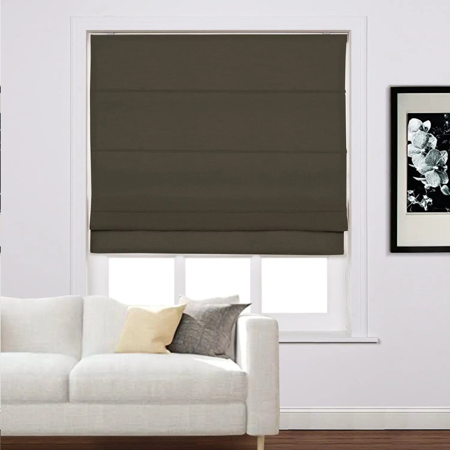 Interior living room featuring a window with a dark brown Roman blind above a white sofa accented with light yellow and grey cushions and a framed black and white botanical print on the wall
