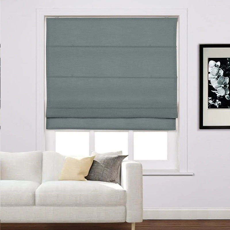 Interior view of a modern living room with a closed teal Roman blind covering a window a white sectional sofa featuring yellow and grey accent pillows and a monochrome floral artwork on the white wall