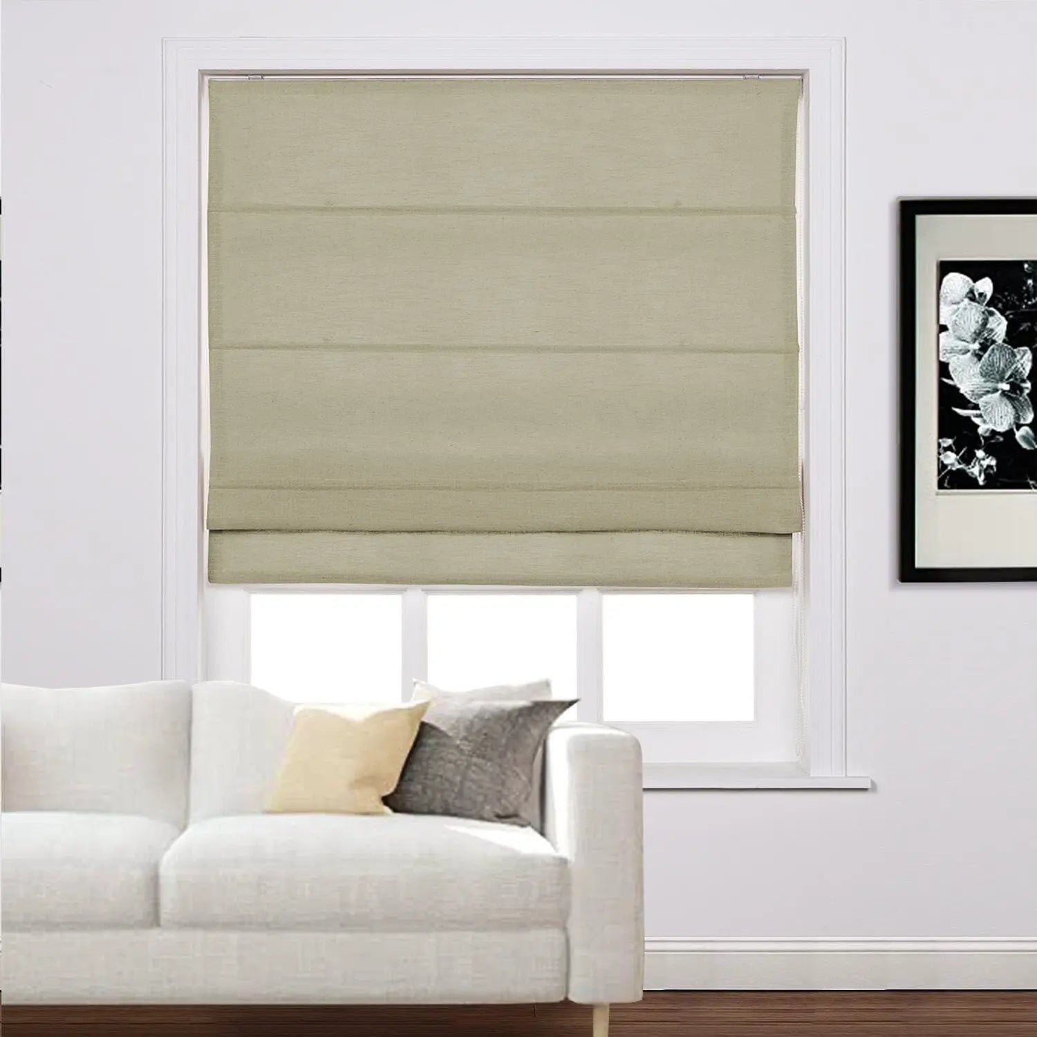 A modern living room featuring a beige textured Roman blind on a white window frame, a crisp white sofa adorned with a yellow and a grey throw pillow, and a striking black and white floral art print on the adjacent white wall above dark wood flooring