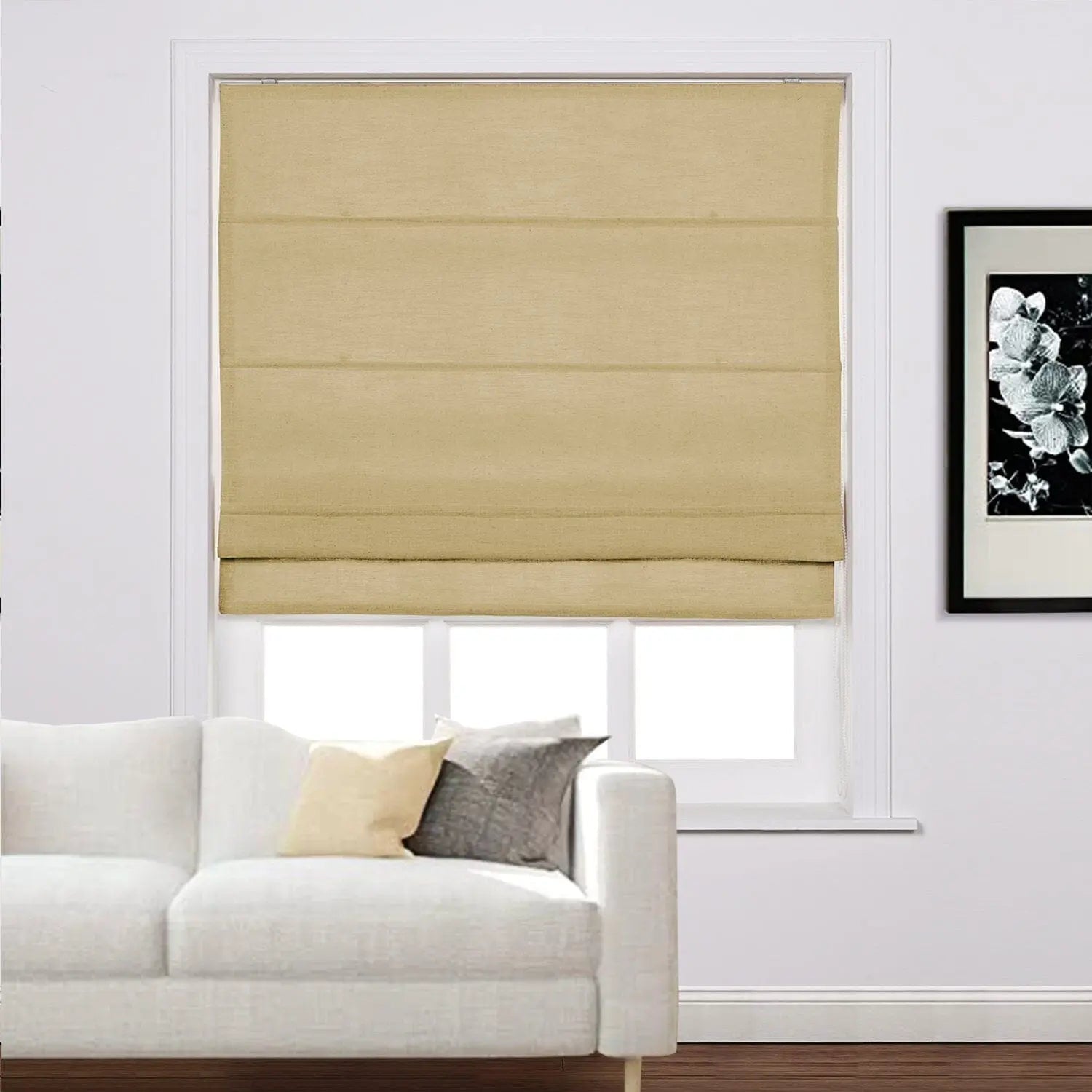 Beige Roman blind installed in a modern living room window above a white sofa with cream and grey accent pillows and a black and white floral artwork on the wall
