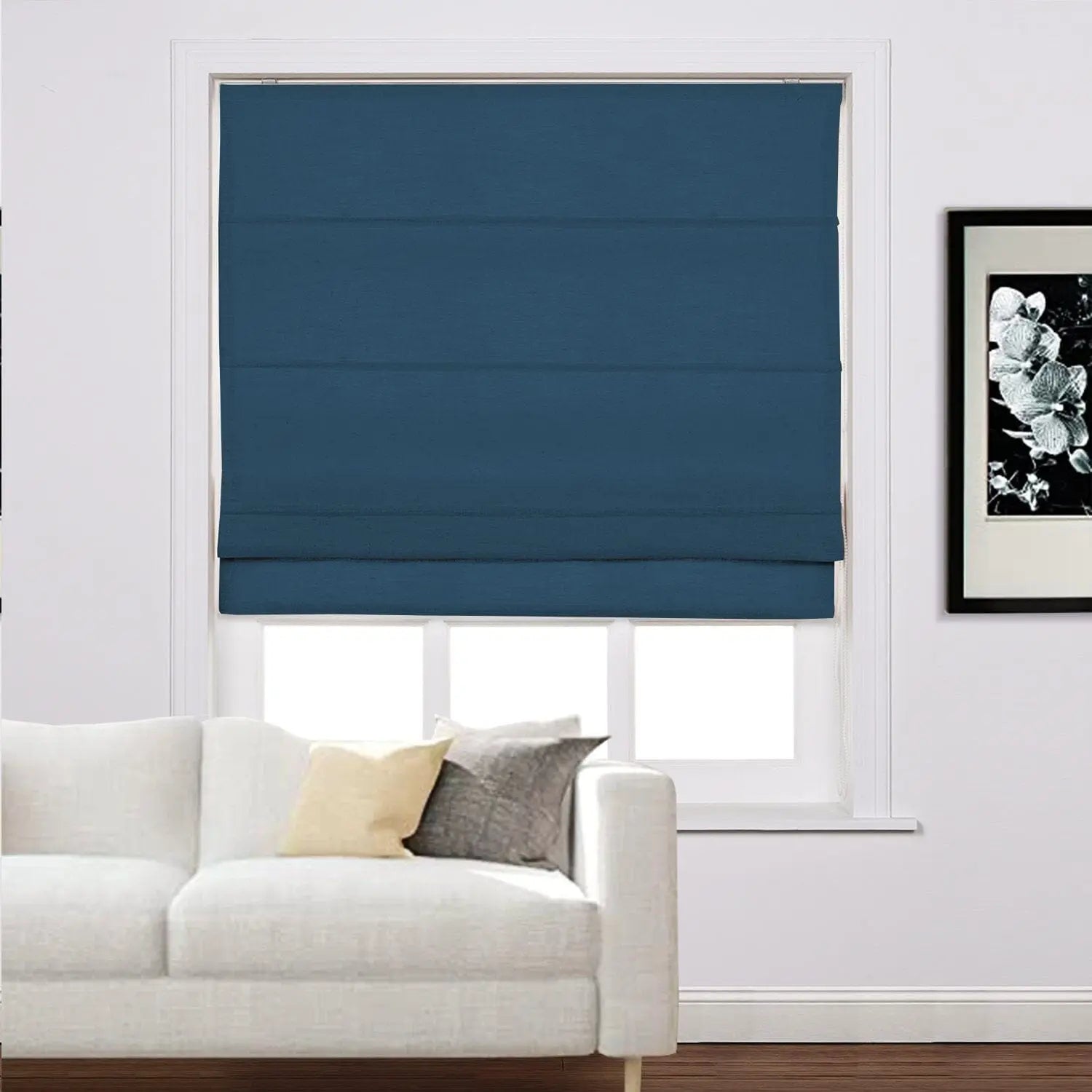 Interior living room scene with a window featuring a deep blue roman blind above a white textured sofa adorned with yellow and grey throw pillows and a black and white floral artwork on the adjacent wall