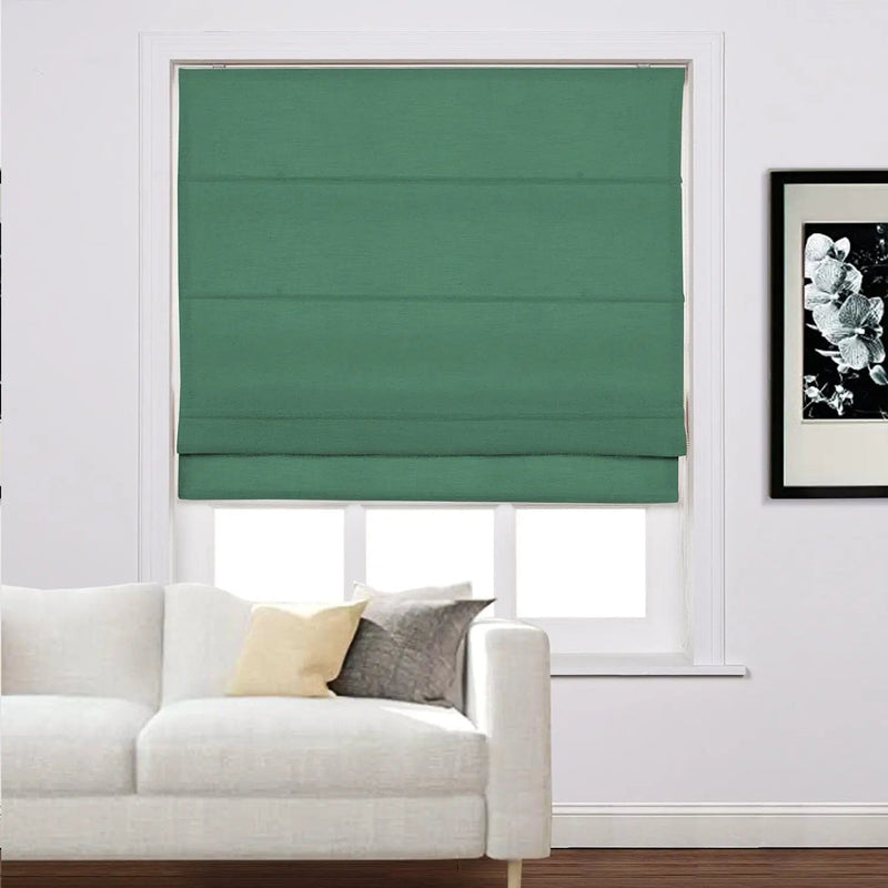 A modern living room interior showcasing a window with a dark green Roman shade, a white fabric sofa adorned with a light yellow and a grey throw pillow, and a black framed black and white floral art print on the wall