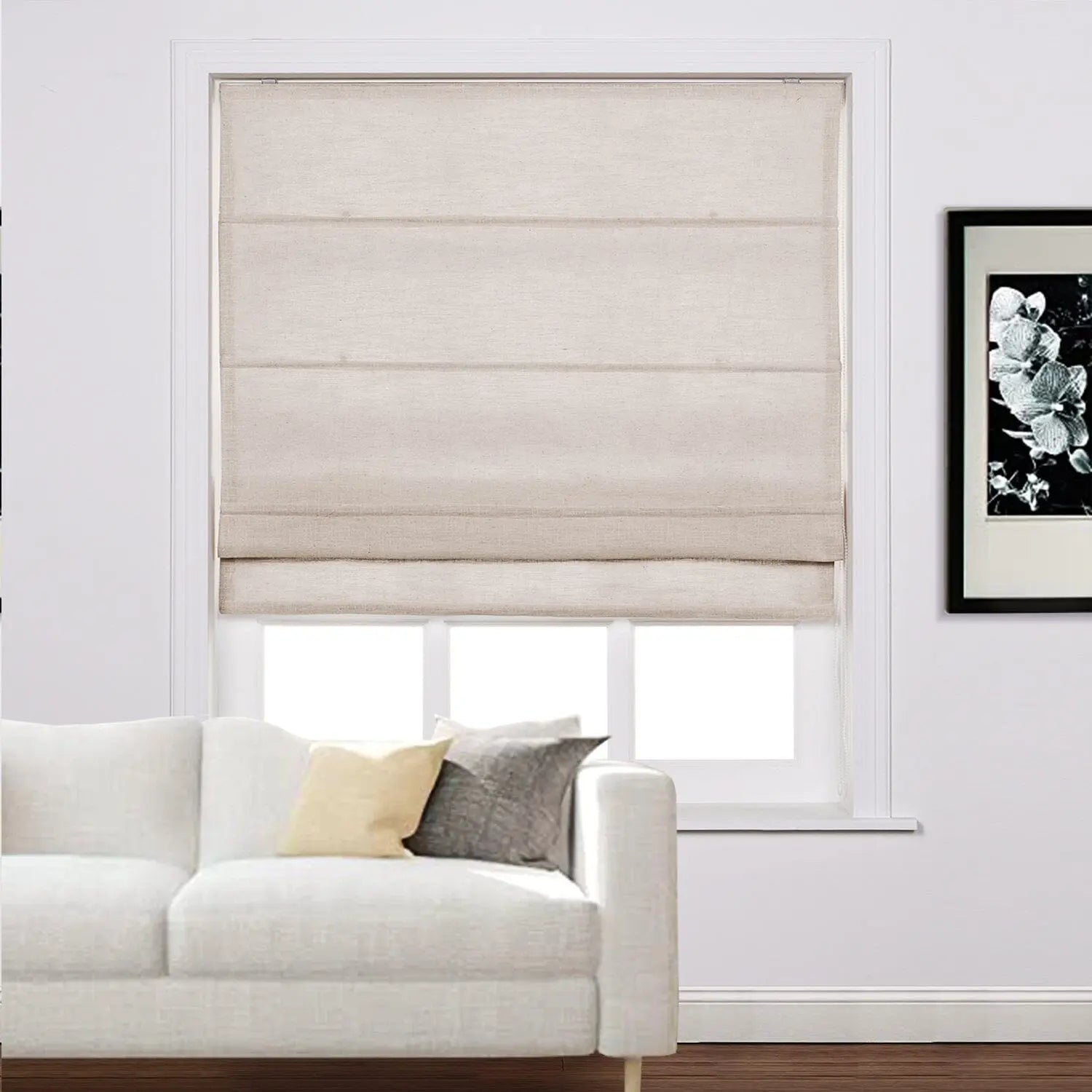 Photograph of a stylish living room featuring a white modern sofa, golden yellow and charcoal gray accent pillows, and a light beige linen Roman blind on the window next to a framed black and white floral art print