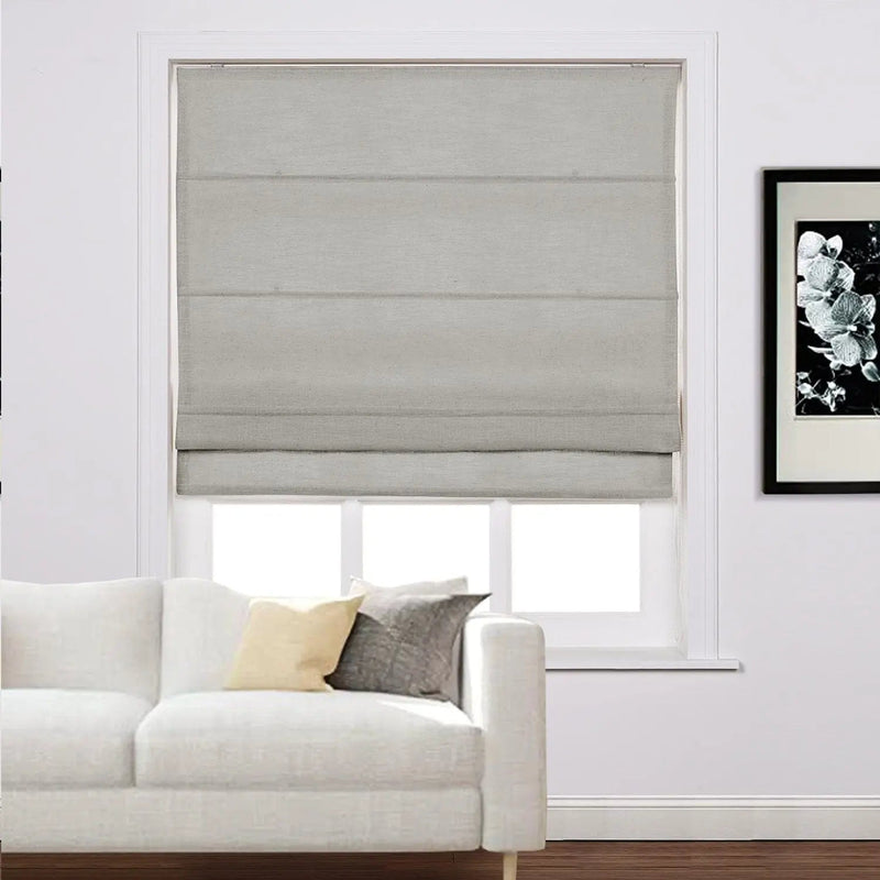Grey Roman blind covering a white window in a modern living room featuring a white sofa with yellow and grey cushions and a framed black and white floral print on the wall