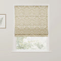 A cream and beige floral patterned Roman blind is lowered in a white window frame, partially revealing a blurred green outdoor view