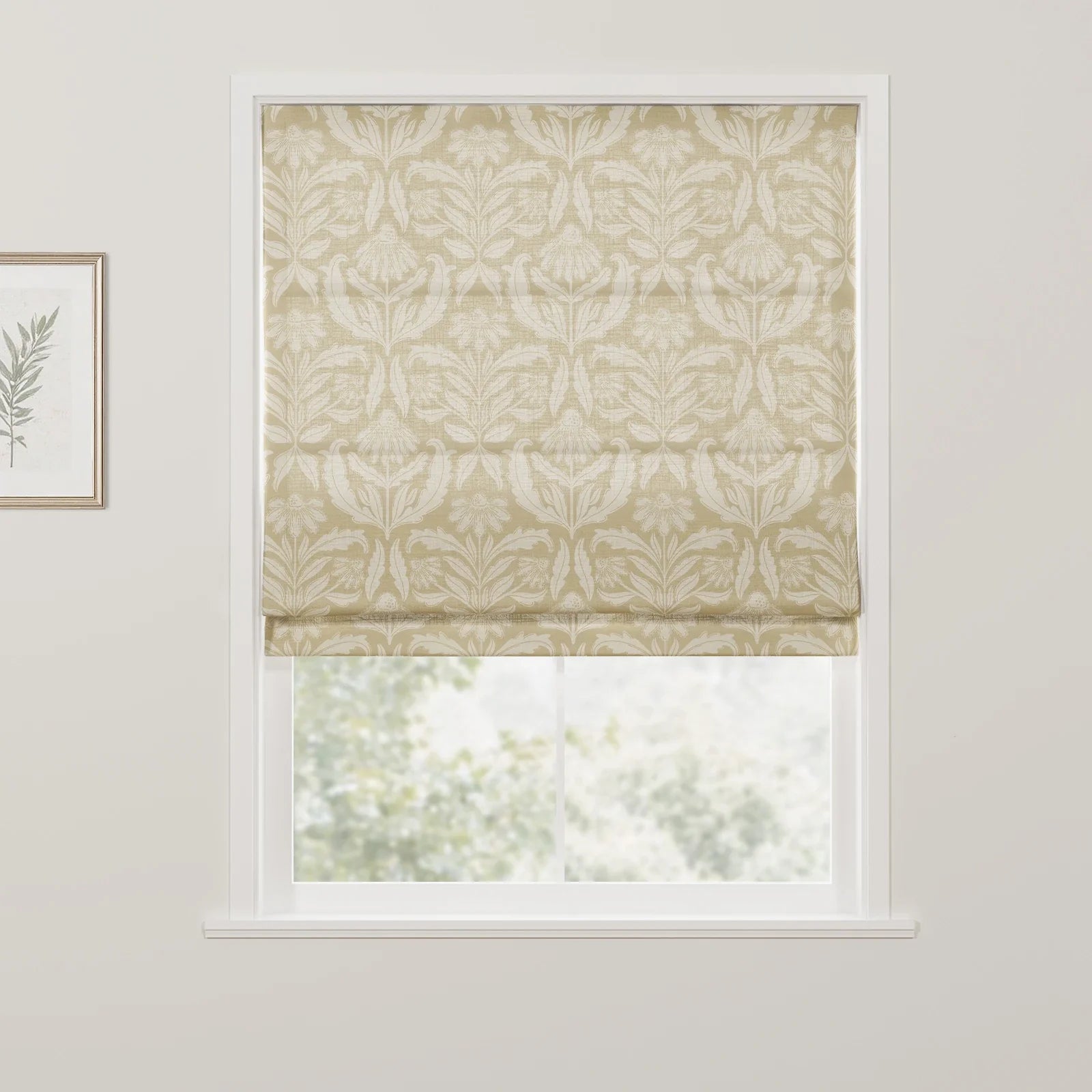 A cream and beige floral patterned Roman blind is lowered in a white window frame, partially revealing a blurred green outdoor view