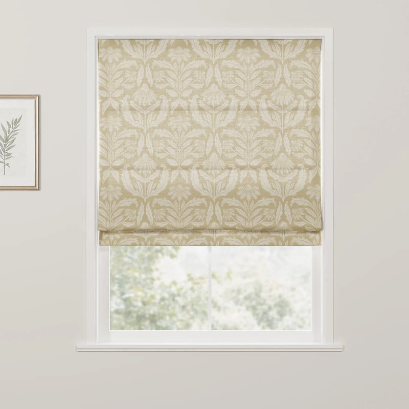 A cream and beige floral patterned Roman blind is lowered in a white window frame, partially revealing a blurred green outdoor view