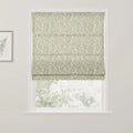 Interior view of a white-framed window featuring a Roman blind with a green willow leaf pattern and a complementary botanical print artwork on the adjacent wall