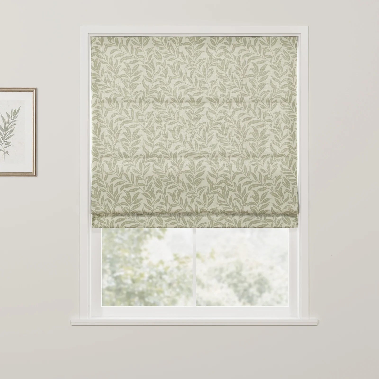 Interior view of a white-framed window featuring a Roman blind with a green willow leaf pattern and a complementary botanical print artwork on the adjacent wall